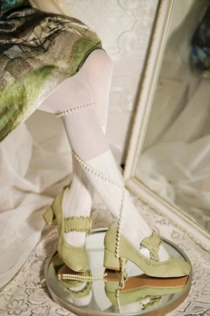 Sage green classic lolita chunky heel mary jane shoes with cutout trim details and decorative bow ankle strap, worn with vintage print skirt and white stockings with pearl ankle chain, low-angle mirror reflection shot