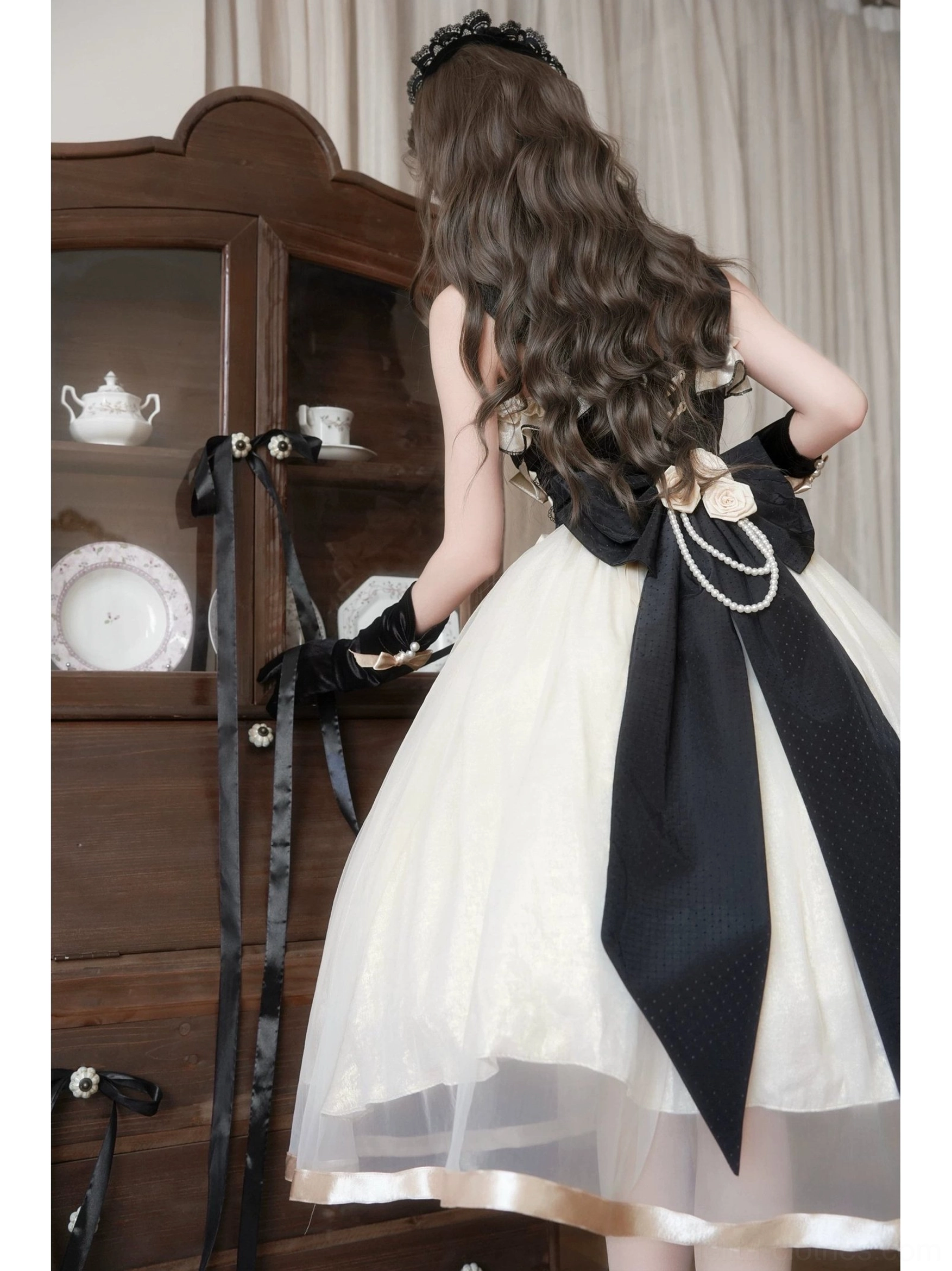 Back view of Classic Lolita jumper skirt featuring dramatic black satin bow with pearl chain accent, flowy tulle skirt with satin hem trim, elegant dress silhouette