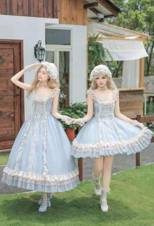Twin models wearing ocean-blue classic lolita JSK dress with white ruffled lace trim and matching lace bonnets, posed in villa garden setting, front three-quarter view showcasing flutter sleeves and rose button details