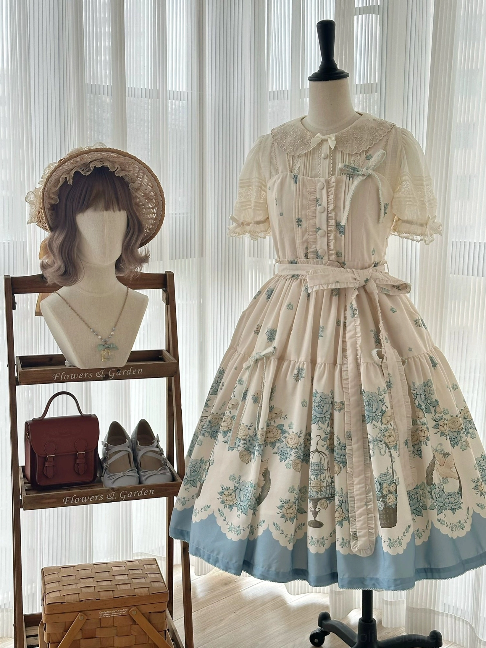 Classic lolita jsk dress three-quarter front view on dress form, blue floral botanical print, short sleeves, scalloped hem trim, coordinated jewelry display