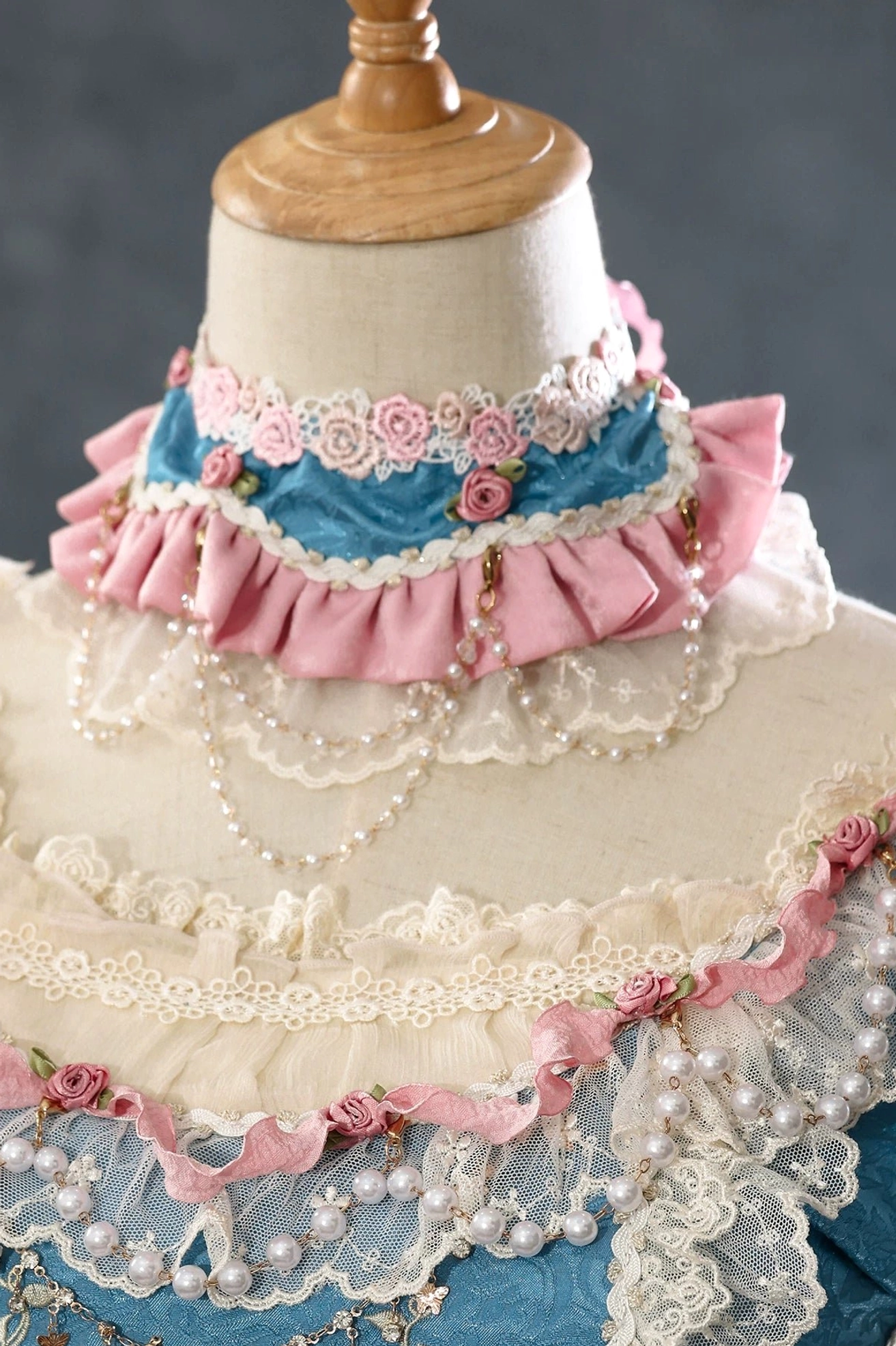 Mint green vintage lolita wrist cuff with beige lace overlay, pink fabric rose and small bow accent on wooden mannequin hand