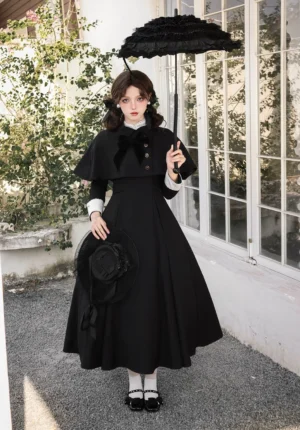 Classic black and white Lolita OP dress with white contrast cuffs and velvet bow, worn with detachable cape, vintage Mary Jane shoes, and lace parasol in outdoor window setting