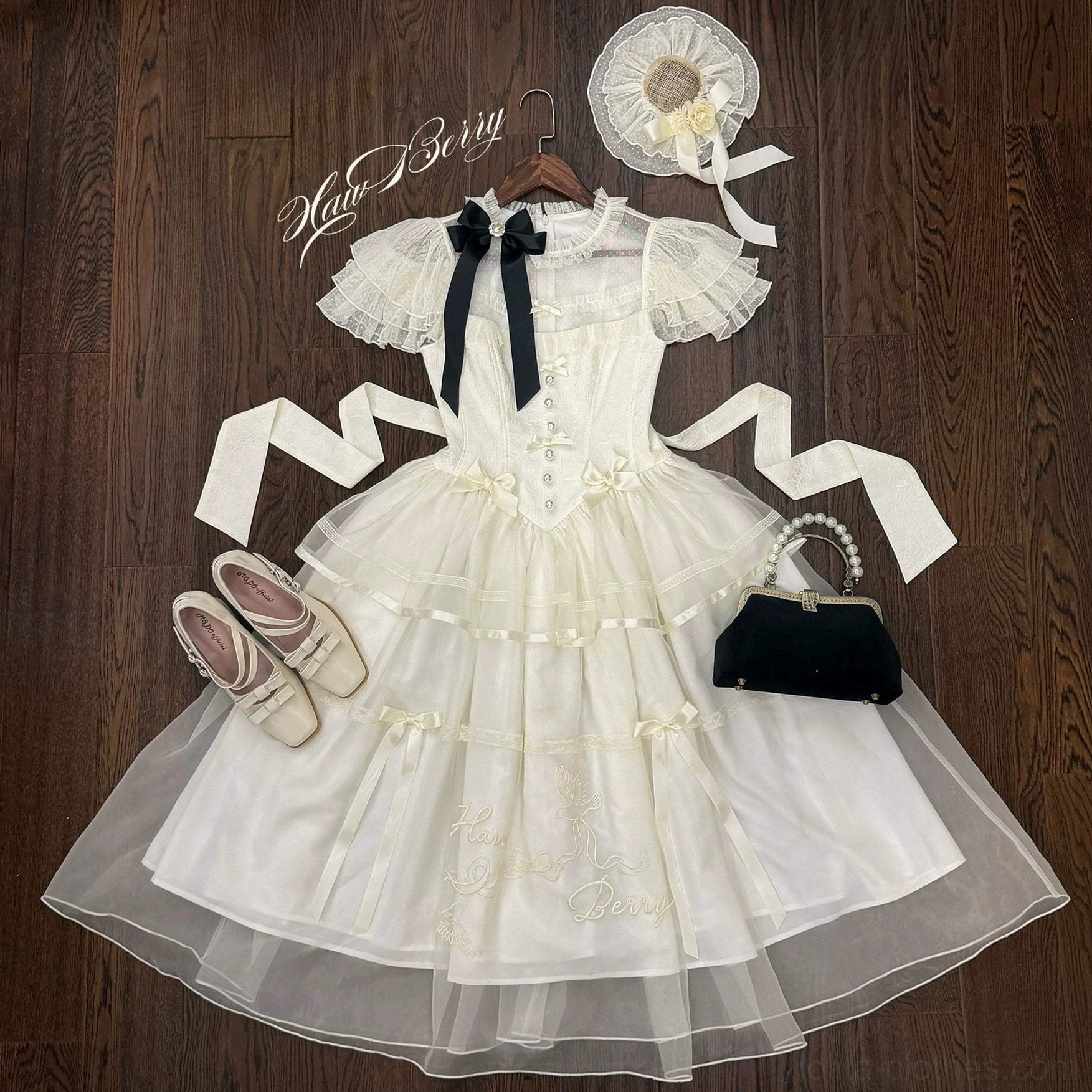 Classic lolita OP dress with matching accessories flat lay display showing embroidered tulle hem, black bow, mini hat, loafers and handbag on wooden surface