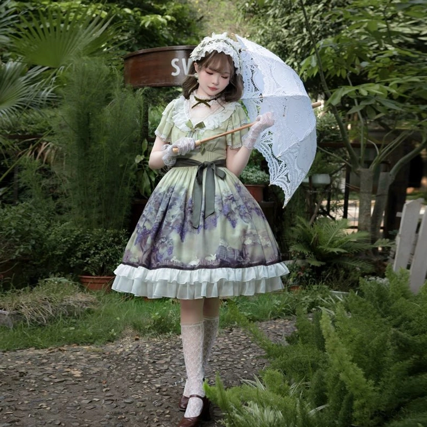 Front full posed view of classic lolita OP dress on model standing garden path with parasol leaning against fence, neat silhouette without gloves, matching hairpiece, grape print and layered ruffled skirt hem