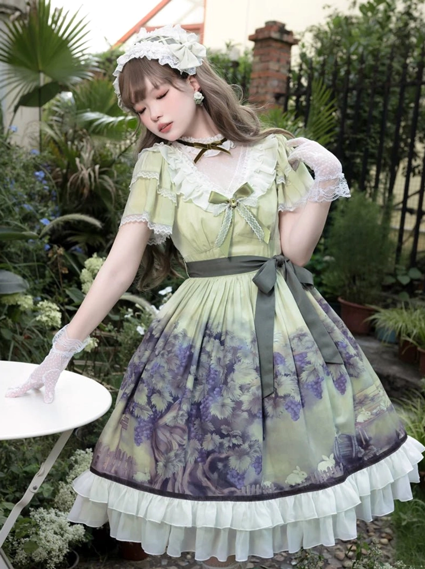 Side three-quarter view of grape print classic lolita dress with model leaning on garden table, featuring V-neck lace overlay, grey waist sash with bow, printed flared skirt and white gloves