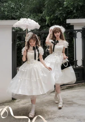 Two models wearing milky apricot classic lolita OP dress with black bow in vintage courtyard setting with parasols and loafers, full-body front view