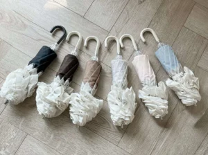 Collection of six folded Lolita parasols in different colors displayed flat lay on wooden floor showing ruffled fabric tie closures and curved J-shaped umbrella handles