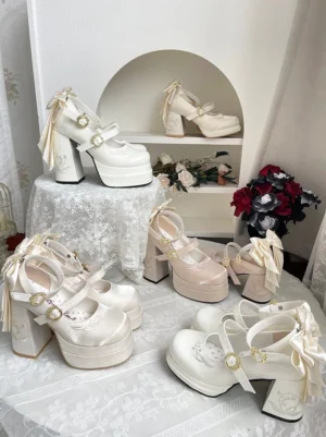 Close-up overhead flat lay of beige and off-white enchanted lolita mary jane platform shoes with oversized back bows, shiny gold-tone round buckles, chunky platform soles and delicate ankle straps arranged on lace tablecloth with red roses