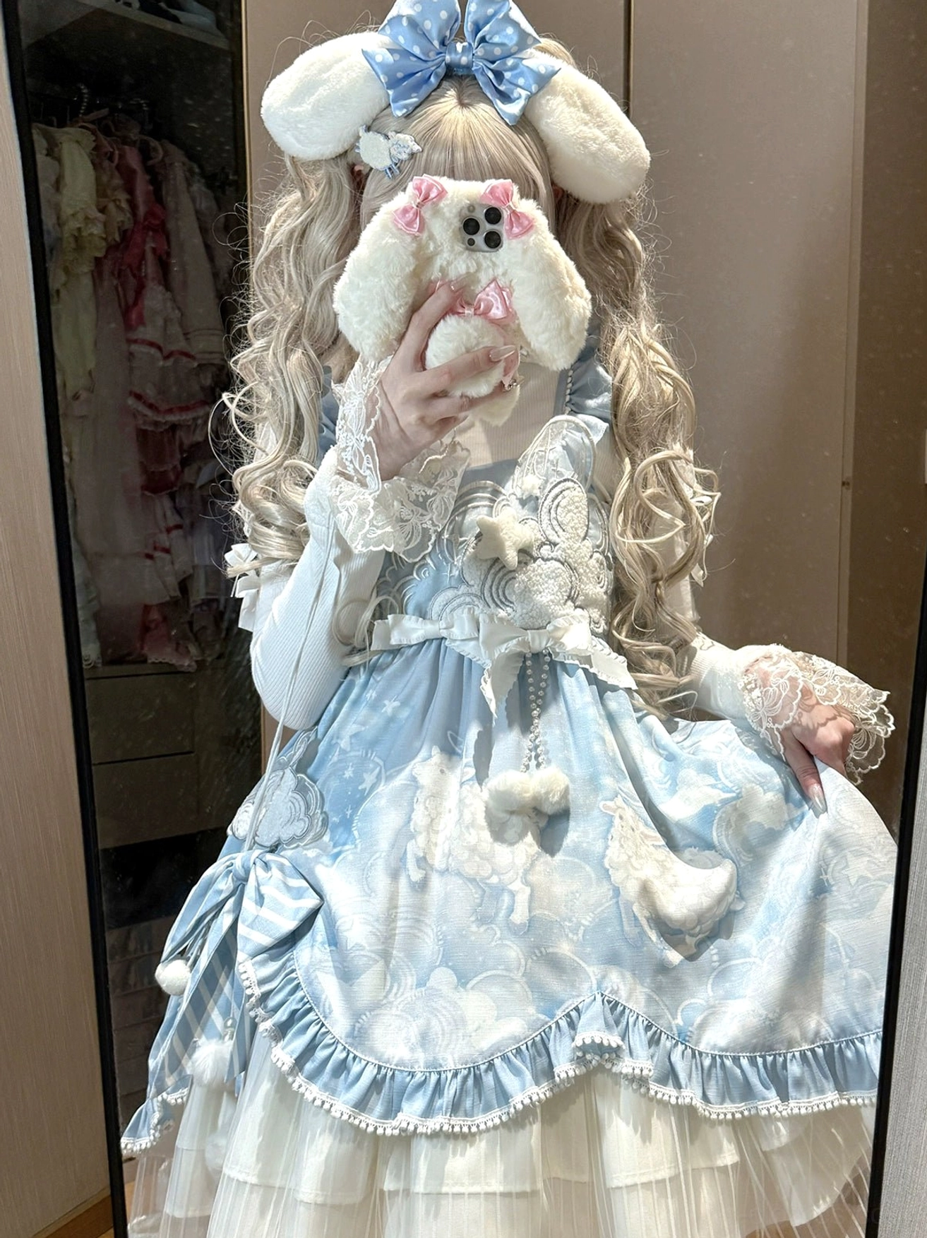Sweet lolita JSK jumper skirt with cloud print in baby blue and off-white, worn by model with blonde twin tails and blue bunny hairbow, featuring fluffy pom-pom decorations and ruffled trims, front mirror selfie view