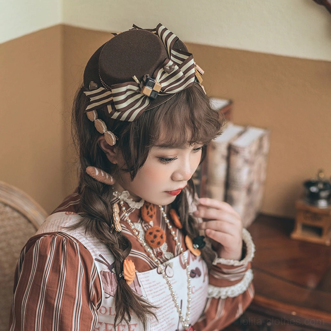 Dark brown coffee hand-made sweet lolita flat-top hat with striped ribbon bow and pretzel cookie-shaped charm decorations displayed on model in side three-quarter vintage study room interior setting