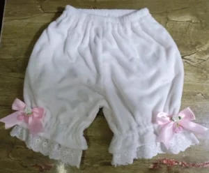 Pink satin bow coral fleece Lolita bloomers flat lay showing delicate floral and berry embellishments on hollow embroidered lace leg cuffs with shirred elastic details on wooden surface