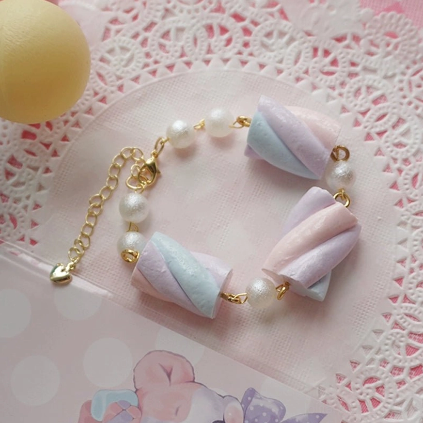 Top-down flat lay view of pastel cotton candy resin lolita bracelet featuring tri-color twisted marshmallow charms with gold metal chain, imitation pearls, and extension clasp on decorative lace doily background