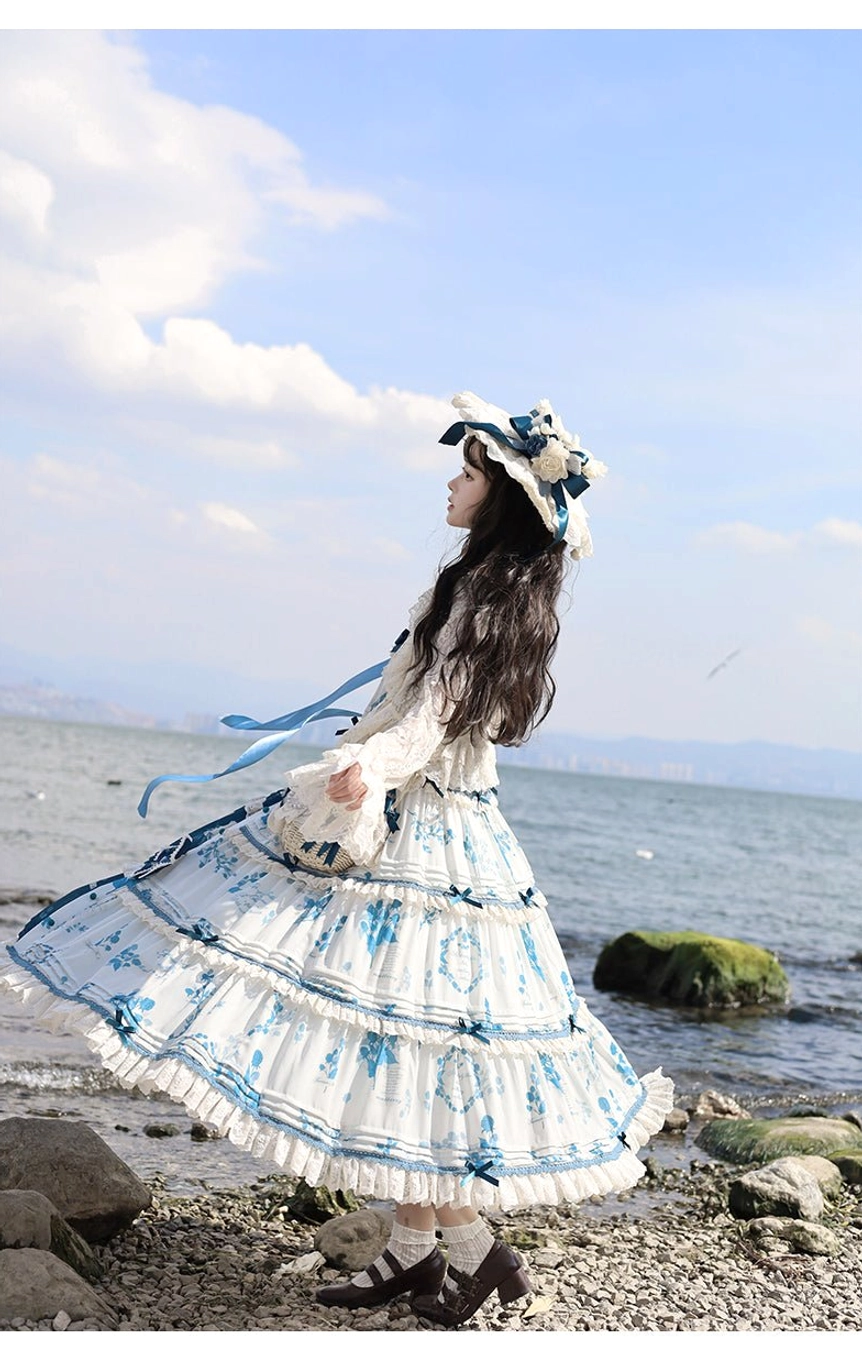 Side full-body perspective of blue and white porcelain print Lolita dress with model twirling layered ruffled hem, straw hat with blue ribbon, and flowing silhouette, photographed at seaside