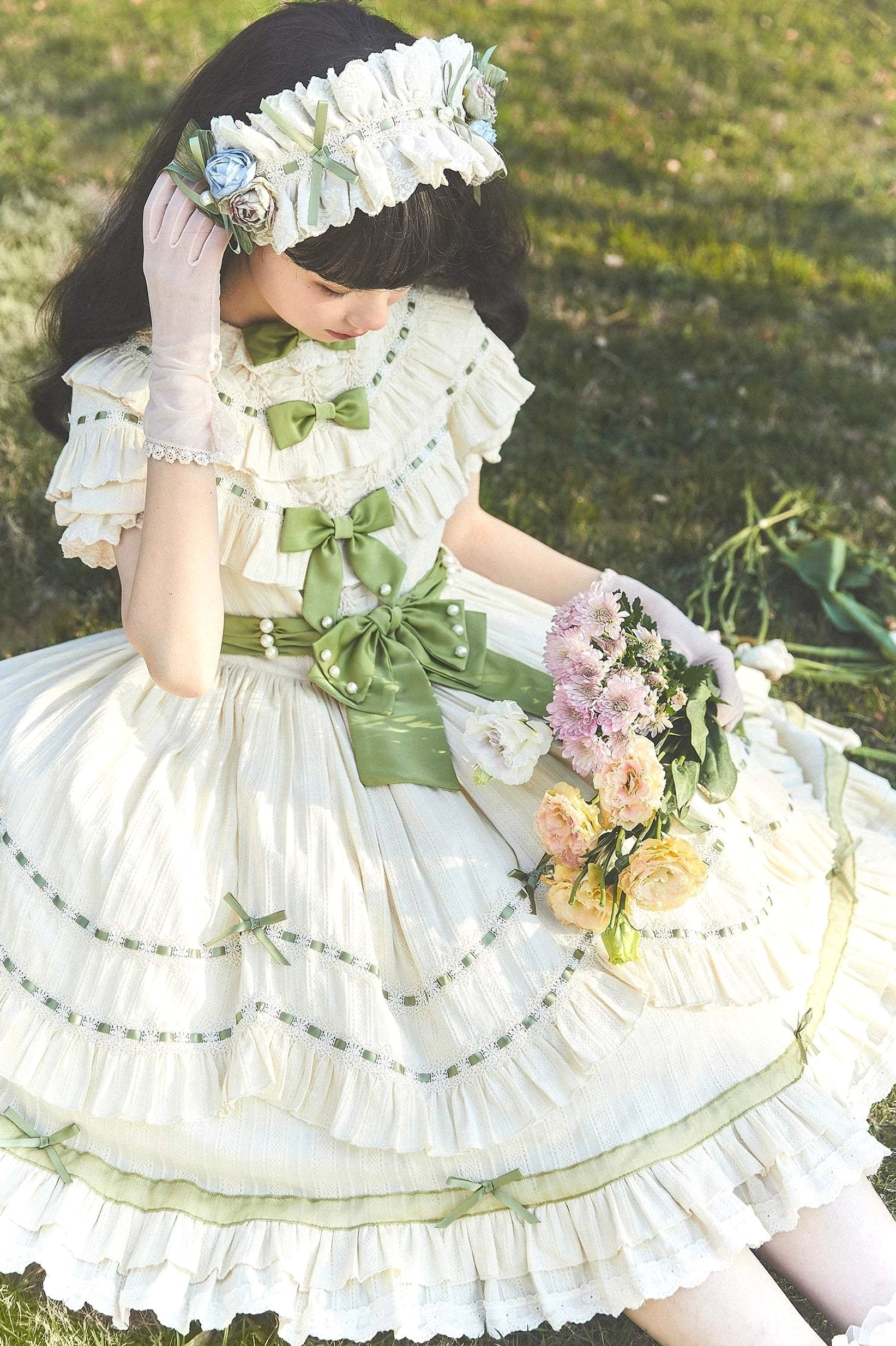 Three-quarter side close-up view of lily of the valley country lolita dress showing frilled neckline with green bows, ruffled hem, green ribbon trims, lace gloves and flower headpiece