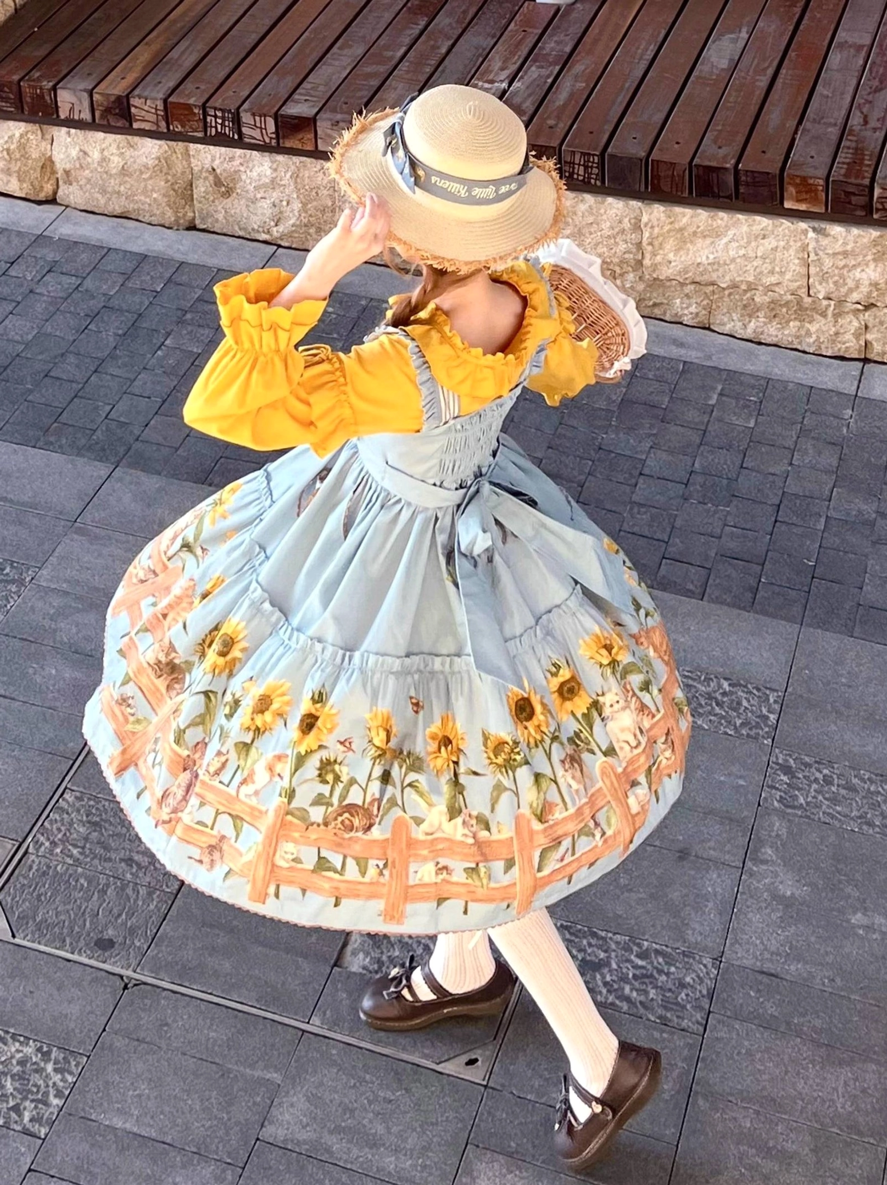 Back three-quarter outdoor view of cat and sunflower country lolita JSK dress showing back shoulder straps and tiered construction