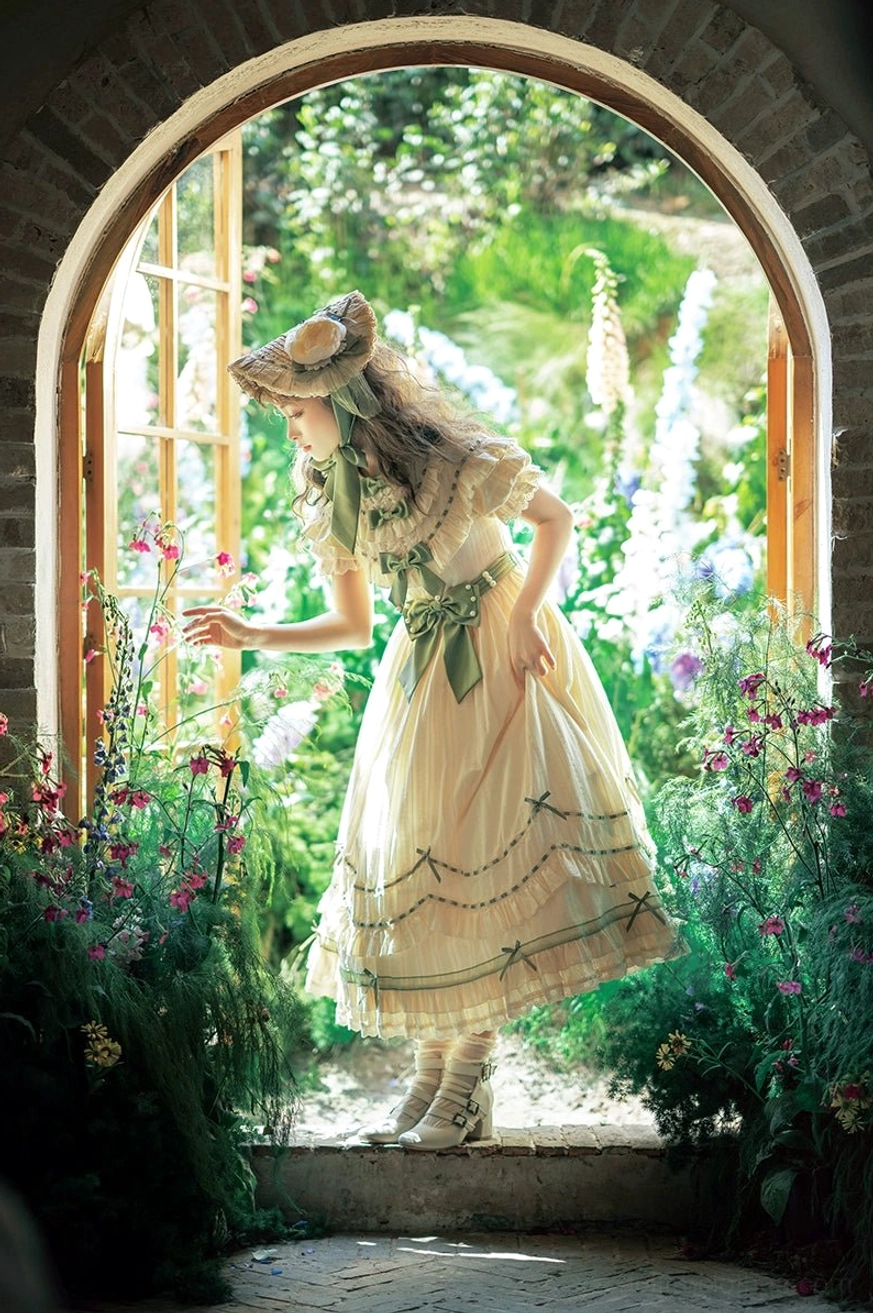 Back view of country lolita OP dress showing green ribbon skirt trims and tiered ruffles worn in outdoor garden archway with floral backdrop
