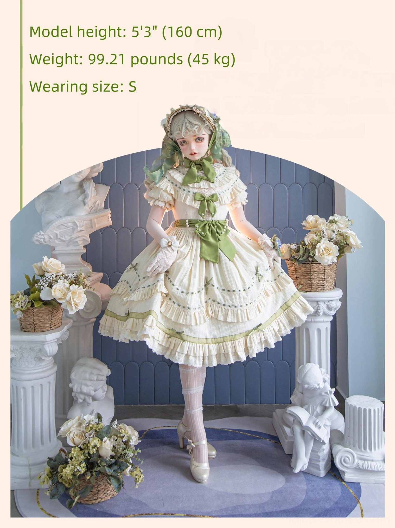 Front standing view of country lolita OP dress with cream base and sage green bows, tiered ruffle skirt, and floral hair accessory in vintage garden statue setting