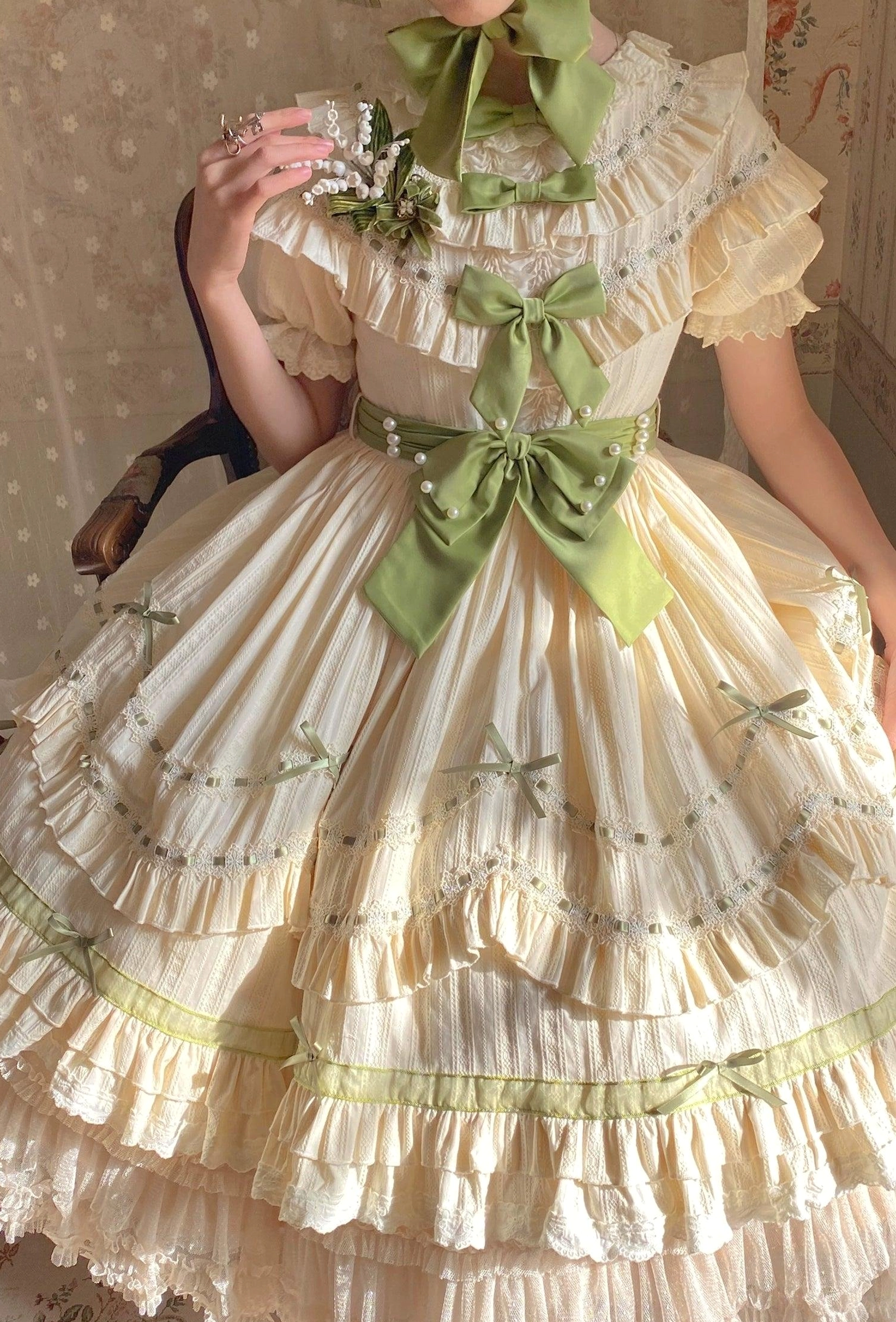Country lolita OP dress with removable waist tie showing cream base, green ribbon trims, and tiered ruffle skirt structure and construction detail