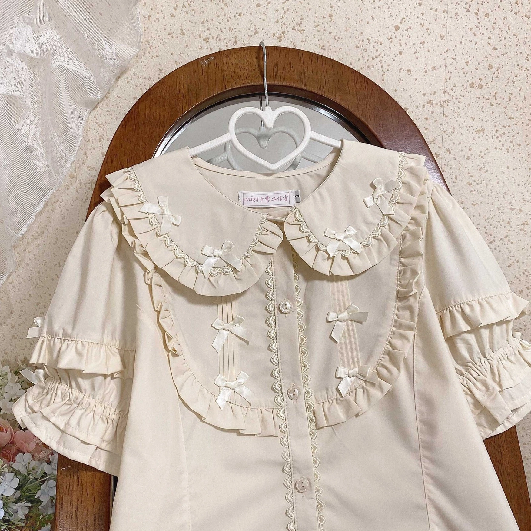 Cream beige lolita short sleeve blouse with ruffled doll collar small satin bows layered puff sleeves front button closure lace trim hanging flat