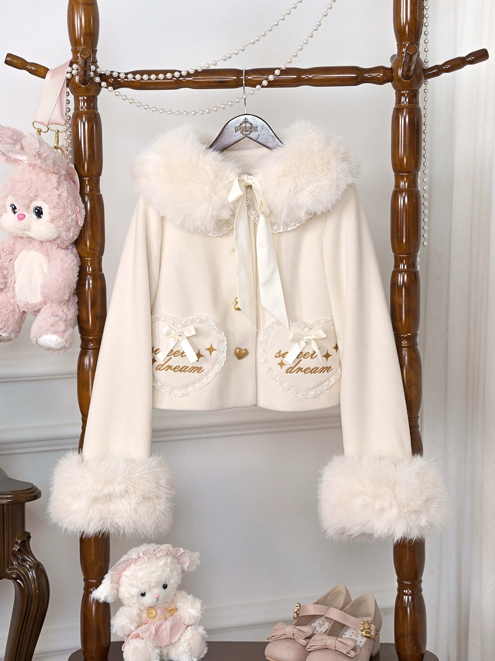 Cream beige fleece-lined sweet lolita coat with embroidered heart pockets and fluffy fur trims, featuring delicate lace and satin bow neck detail, on wooden rack
