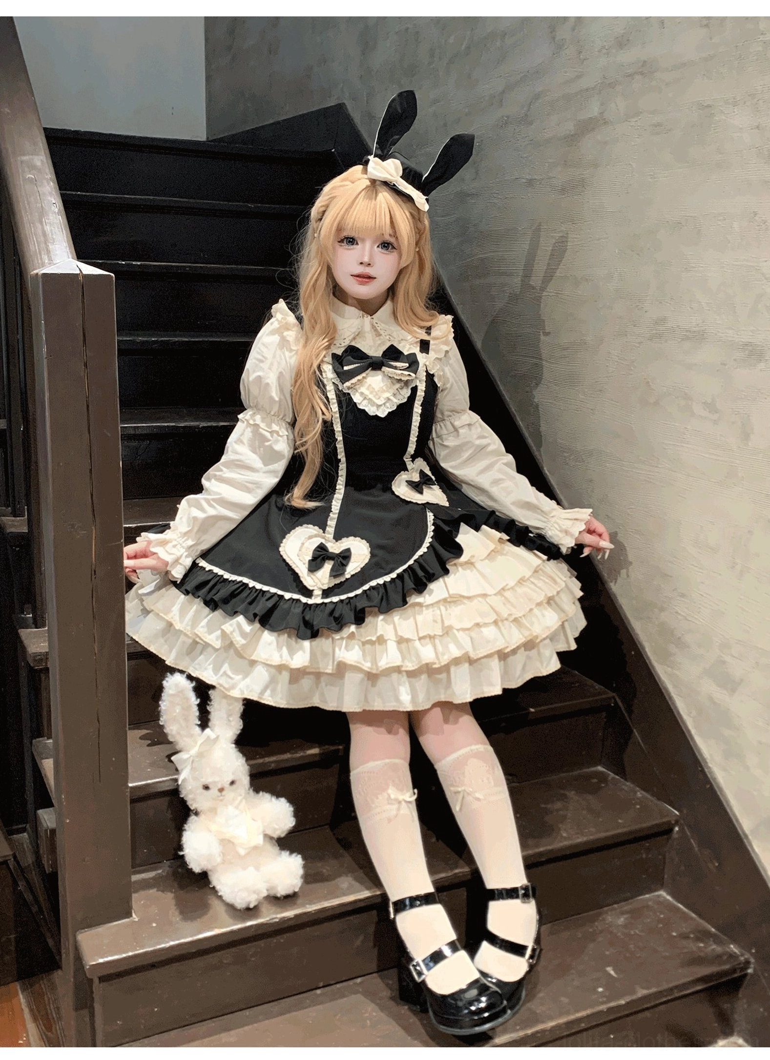 Cream Bud tiered hem old school lolita JSK black colorway front three-quarter seated view with stairwell backdrop and plush rabbit prop