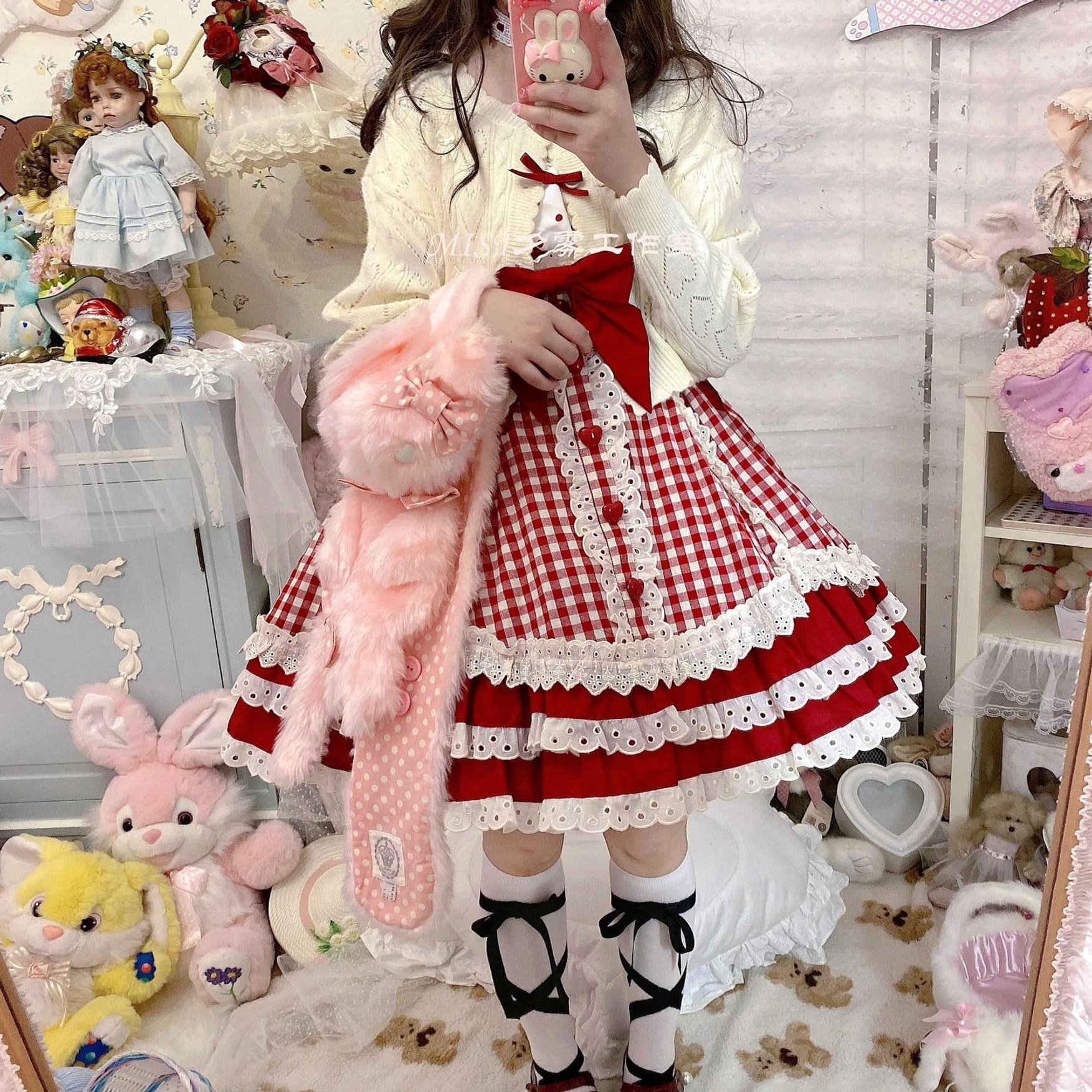Cream hollow out long sleeve Lolita cardigan worn by standing female model with red gingham tiered Lolita dress, bedroom filled with dolls and plush toy accessories