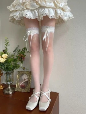 Lolita over-the-knee sheer lace stockings with cream satin bow details worn with frilly skirt and cross-strap Mary Jane heels front full leg view