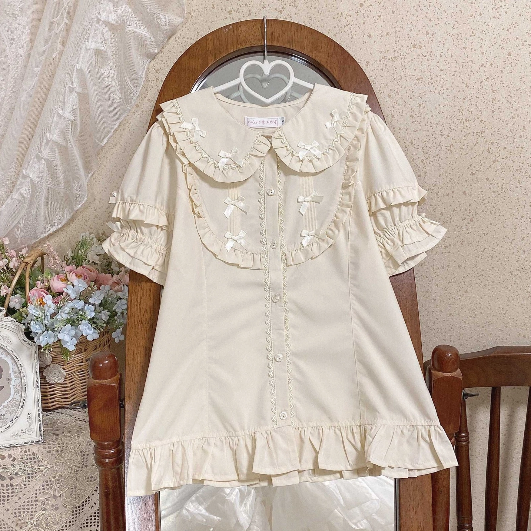 Cream beige lolita short sleeve dress with ruffled doll collar front mini satin bows hem ruffle trim simple button front design on wooden hanger