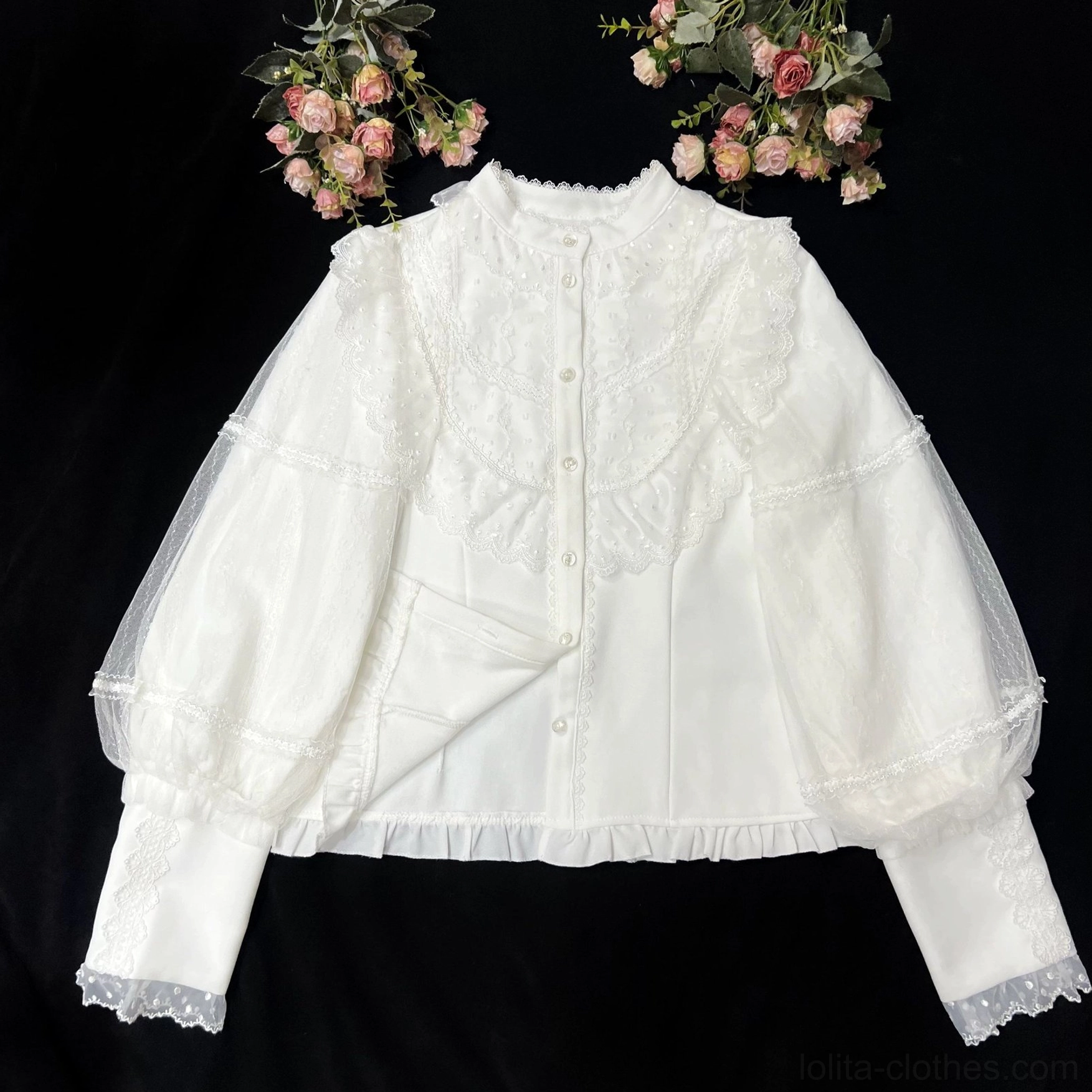 Standalone flat lay of cream vintage Lolita blouse on black background showing ruffled stand collar, front button placket, embroidered lace chest panel, sheer lantern sleeves with lace-trimmed cuffs, and ruffled bottom hem with pink flower bouquets