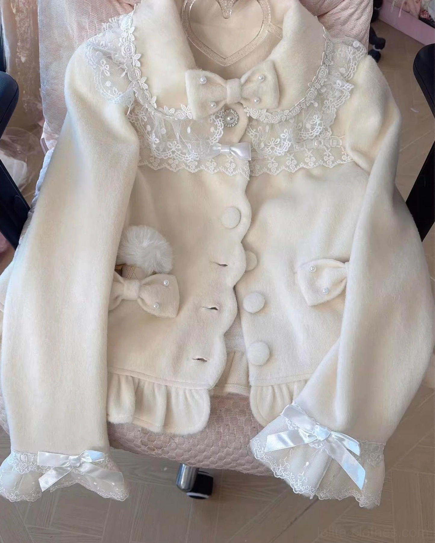 Cream-colored lolita wool coat flat lay display with lace peter pan collar detachable bow ruffled hem and pom-pom pocket decoration