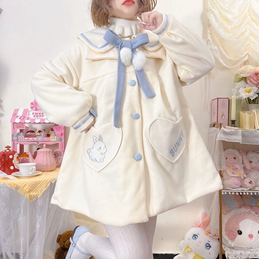 Cream off-white plus size sweet lolita wool winter coat full-body front view worn by model in pink doll room with blue sailor collar bow white pom-poms heart bunny embroidered pockets and blue buttons
