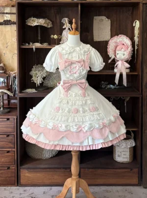 Cream rosette cake old school lolita JSK dress front view showing white base with soft pink polka dots, 3D rose decorations, puffed short sleeves, and front decorative bows on wooden dress mannequin display