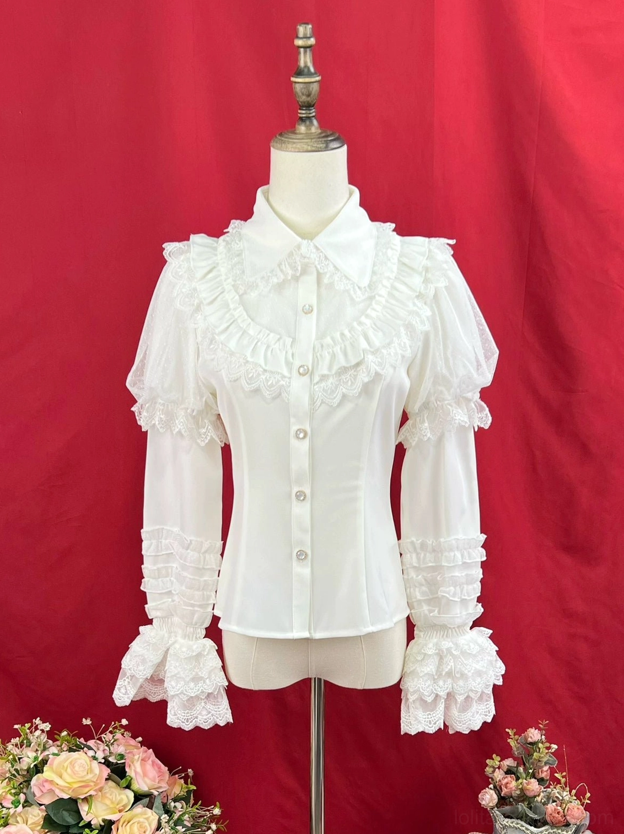 Cream white sweet lolita long sleeve blouse with peter pan collar front pearl button closures chest lace ruffle trim and layered flared lace cuff on dress form red studio backdrop with flowers