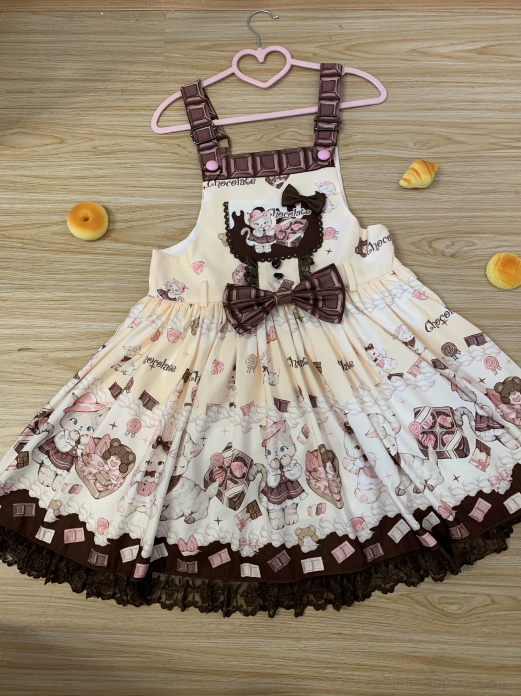 Cream yellow and brown kawaii cat print Lolita salopette dress featuring multi-layered skirt panels, lace trim details, front waist bow, and chocolate print straps showcasing sweet lolita summer aesthetic design elements
