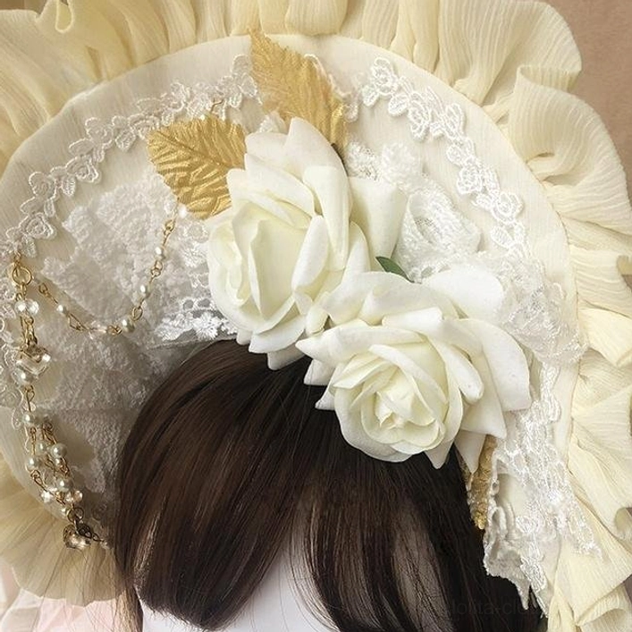 Front close-up view of cream yellow rose-decorated sweet Lolita BNT bonnet with ruffled trim, white artificial roses, gold leaf decorations, and pearl chain lace trim displayed on dark brown wig mannequin
