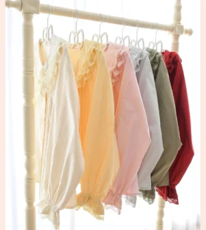 Multiple color variants of daily Lolita long-sleeve blouses displayed together on wooden clothing rack with soft lighting, showing six solid color options with simple ruffled cuffs and cotton fabric construction