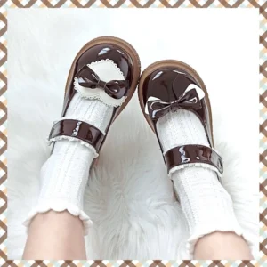 Dark brown glossy Lolita Mary Jane shoes worn on-foot with frilly white socks, displaying small bow heart-shaped lace trim and ankle buckle strap against fluffy fur background