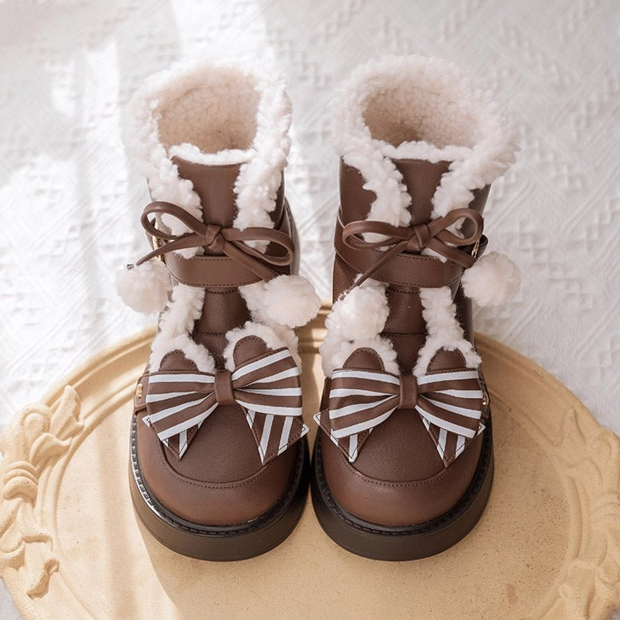 Top-down flat lay of dark brown lolita snow boots with fuzzy fur collar pom-pom trim striped front bow and smooth leather upper on gilded decorative tray