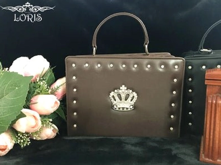 dark brown studded gothic lolita crown handbag front flat lay metal round studs perimeter silver crown ornament rigid top handle dark backdrop floral wooden accents