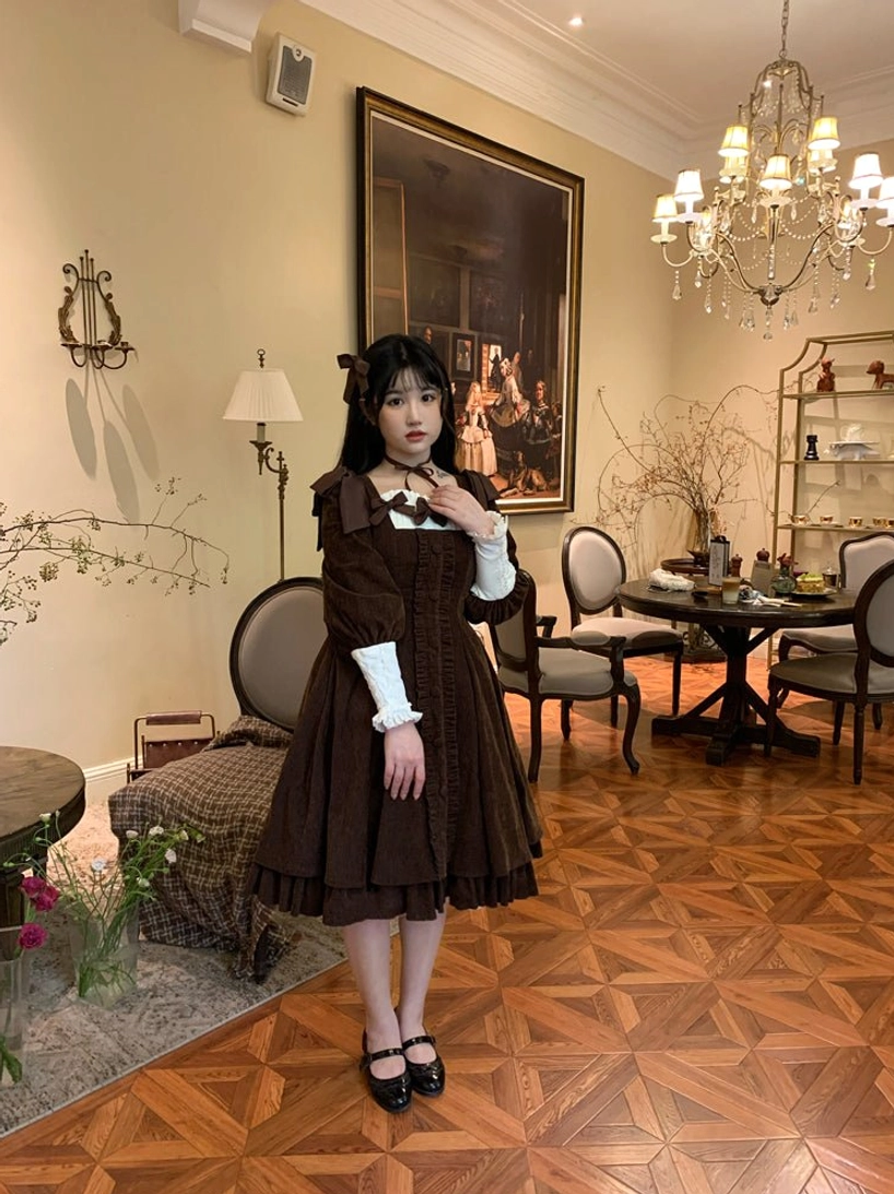 Dark brown velvet Lolita OP dress full-body standing portrait in retro European-style dining room, featuring square neckline with contrast white detachable cuffs and simple chest bow trim