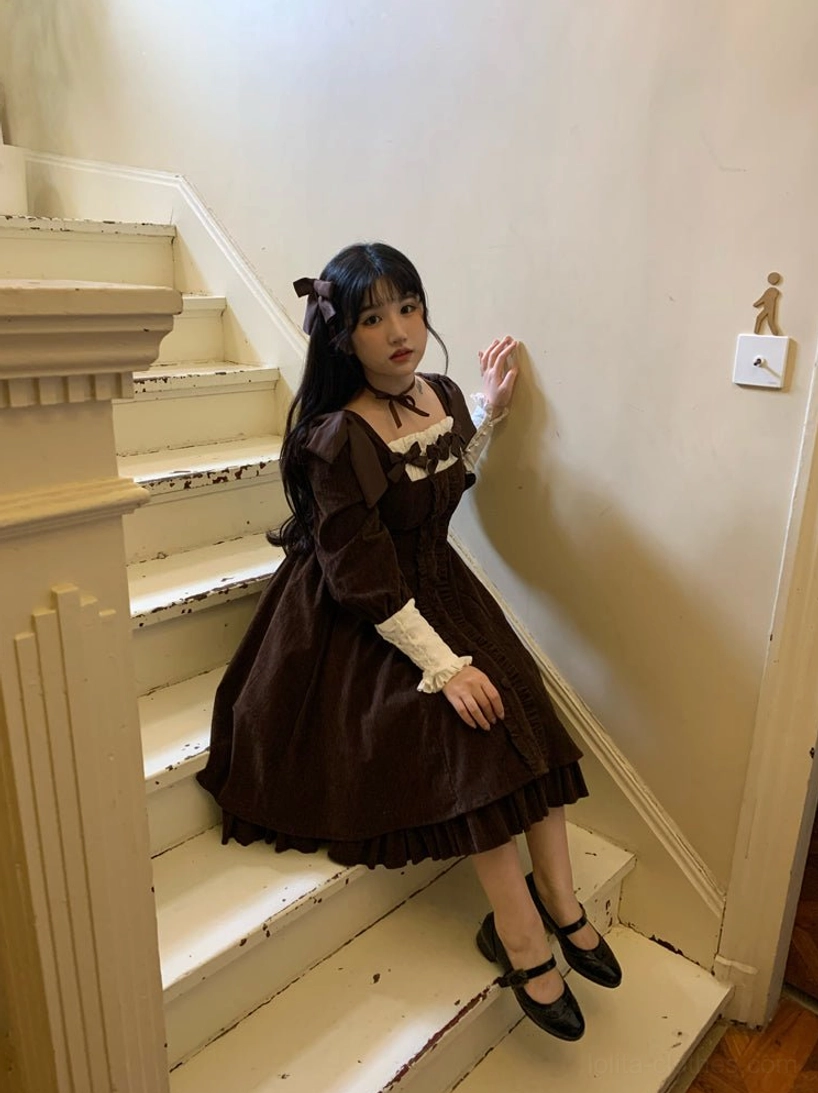 Dark brown velvet Lolita OP dress half-body sitting stair shot in vintage minimalist stairwell, showing ruffled skirt hem, contrast white cuffs, and matching brown hair bow accessory