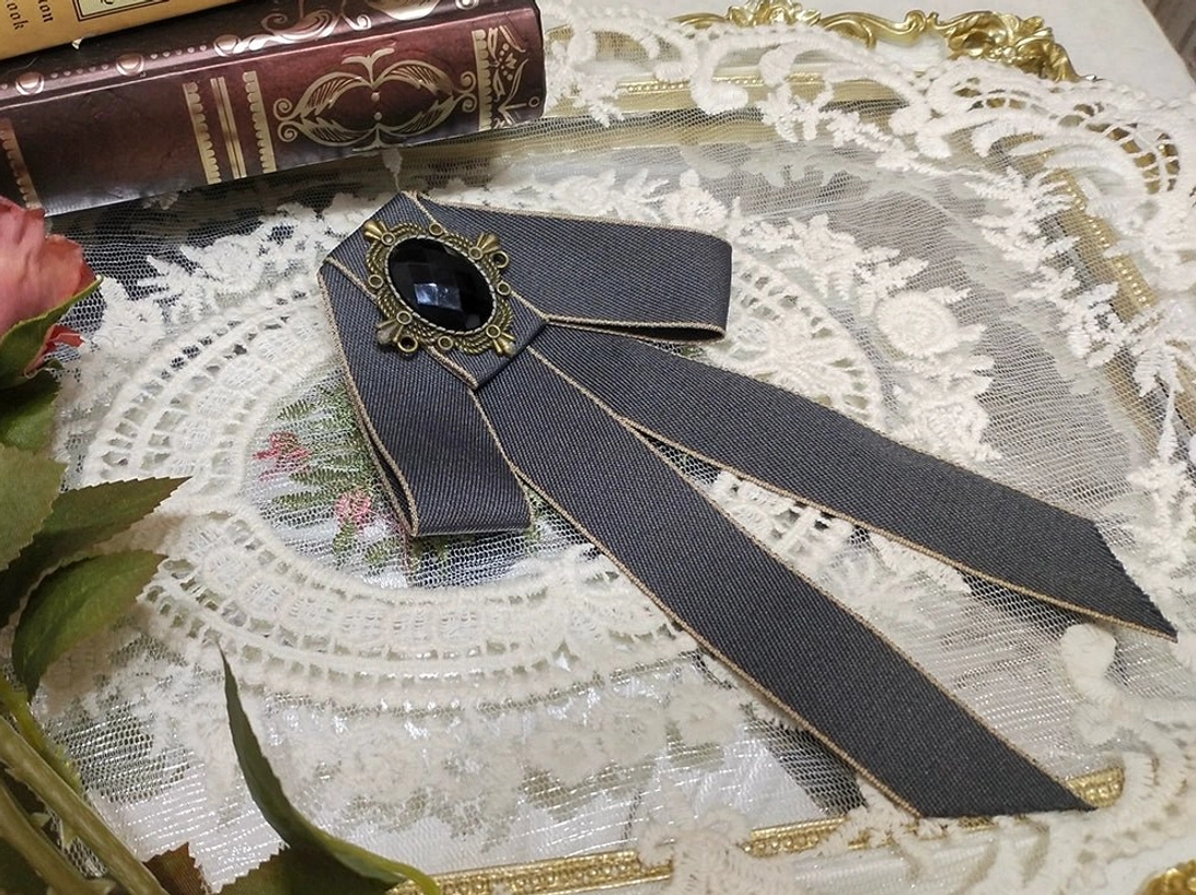 dark-gray-lolita-ribbon-bow-brooch-gold-edge-trim-oval-black-gemstone-bronze-setting-white-lace-doily-green-foliage-vintage-books
