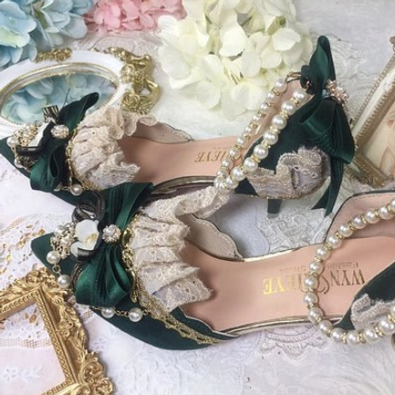 Dark forest green pointed toe Lolita wedding heels overhead flat lay on vintage lace cloth, featuring green satin bow decor, intricate lace ruffles, pearl and gold trim details