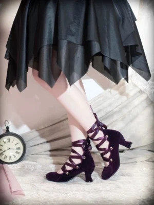 Dark purple velvet lolita lace-up heels with crisscross satin ankle straps and block heel design, shown in low side view on model's feet paired with black irregular hem lolita skirt and vintage pocket clock bedroom setting