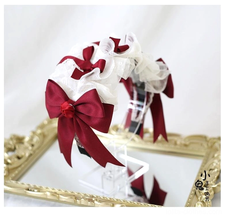 Dark red lolita headband accessory three-quarter side flat lay view on golden mirror tray background featuring white ruffled lace base with large wine-red satin bow and central flower decor