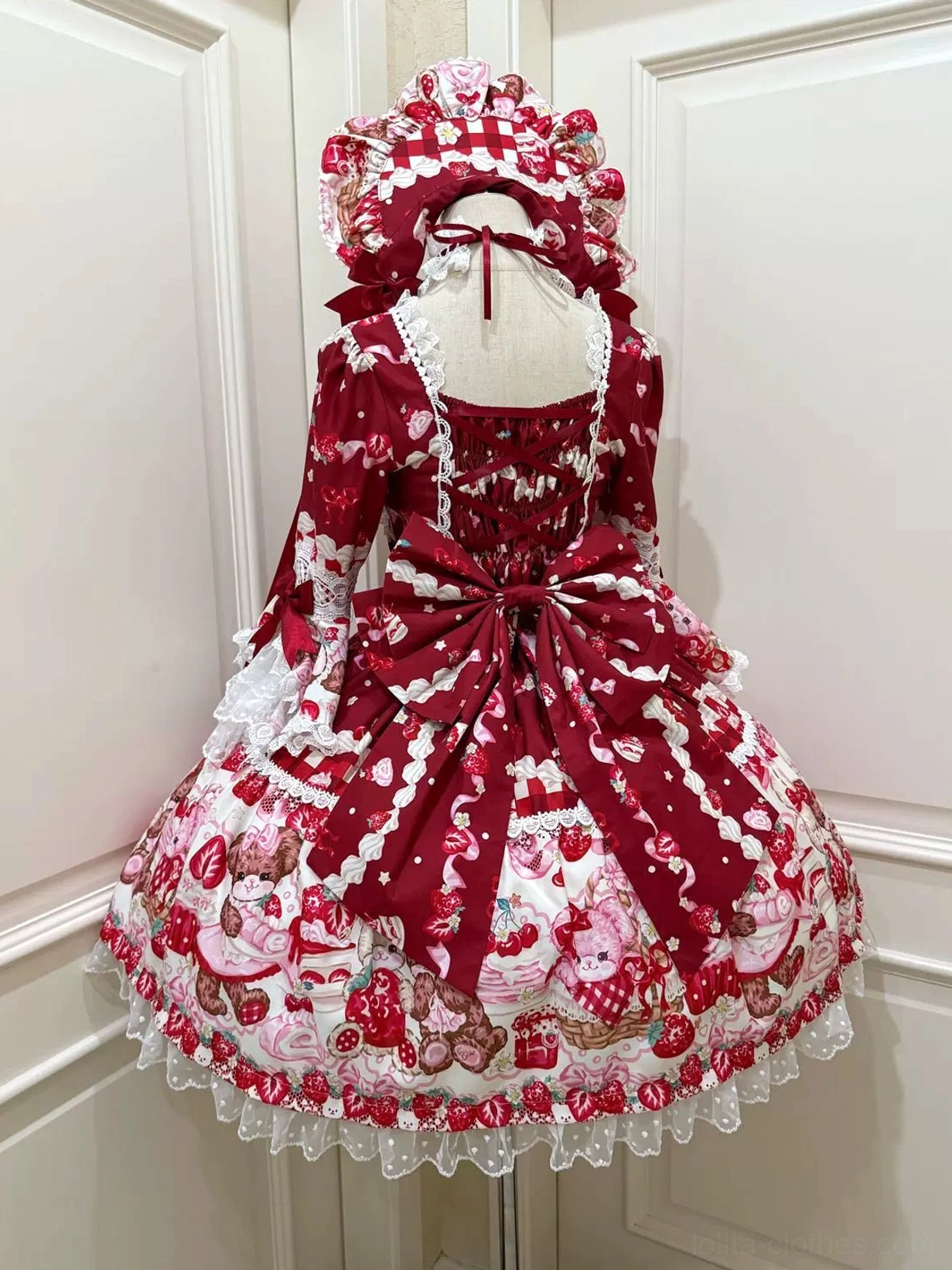 Deep red sweet lolita OP dress back view on mannequin showing crisscross lace-up back, extra large red satin waist bow, ruffled hem with white lace trim and matching bonnet