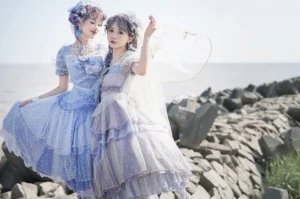 Enchanted Deep Sea Lolita one-piece dress in two color variants - light blue and lavender gradient - shown on two standing models at seaside breakwater with ruffled tiered skirts