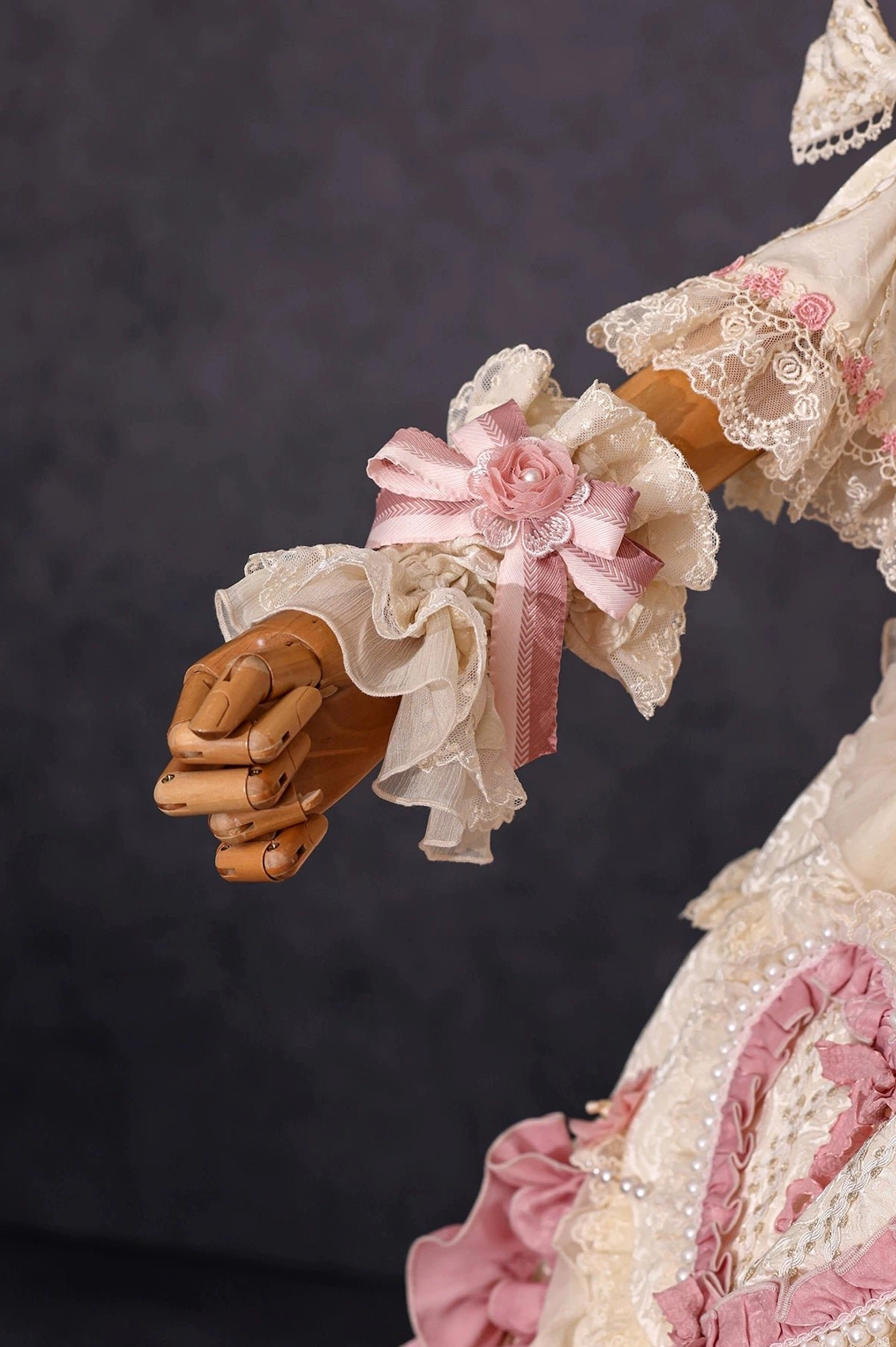 Neutral beige lace lolita wrist cuff with tiny pink fabric rose and ribbon bow accent on wooden mannequin hand