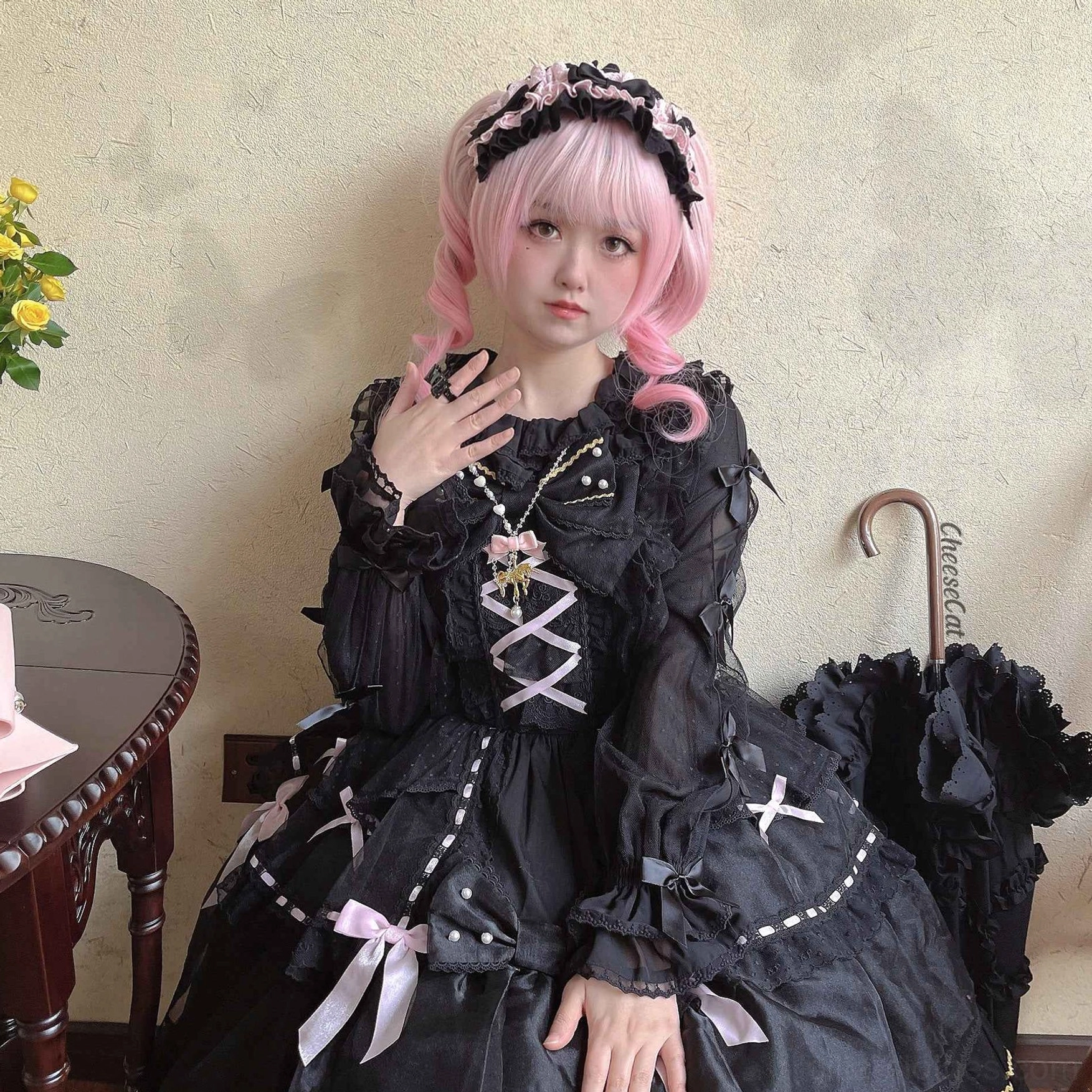 Classic black cotton lolita headdress with matching black tiered ruffled dress on pink wig model in outdoor wooden patio setting showing full coordinate with fishnet stockings and satin bow accents