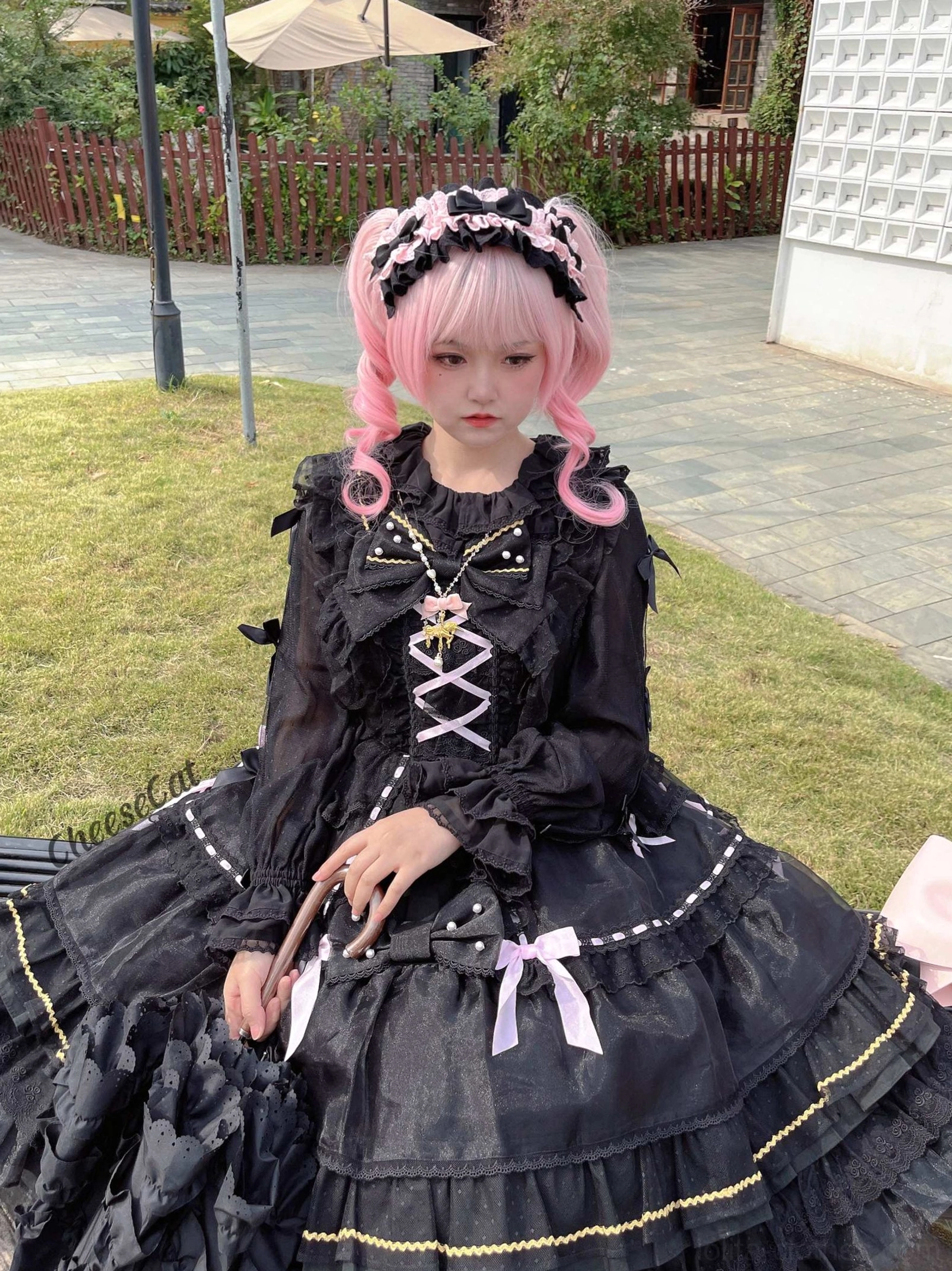 Black lace cotton lolita headdress with white trim and delicate bow accents shown in close-up front view on pink wig model at indoor flower table backdrop demonstrating fitted construction